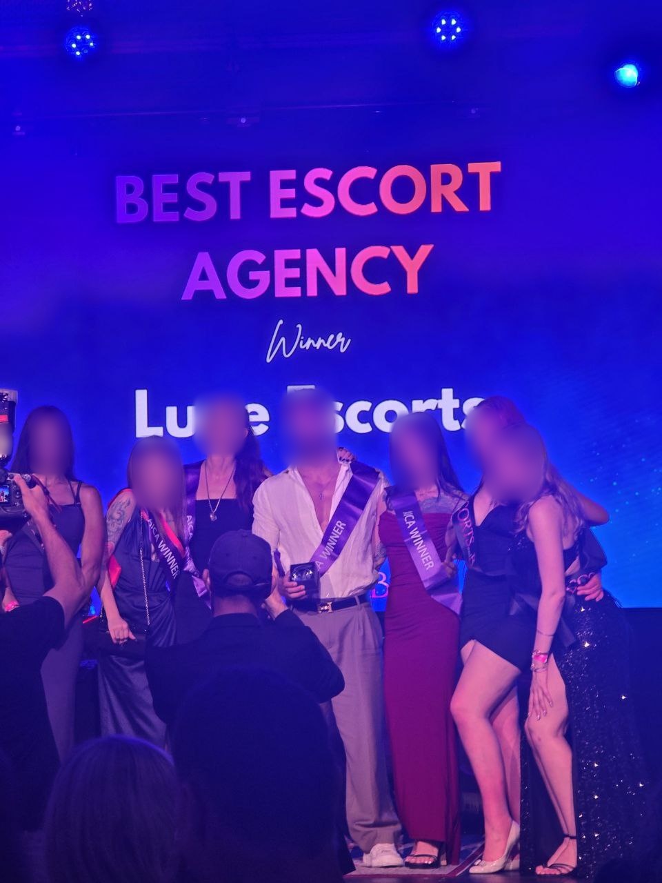 uxe Escorts team standing on stage with winner sashes, posing in front of a “Best Escort Agency – Winner” screen at the Australian Adult Industry Choice Awards 2025.